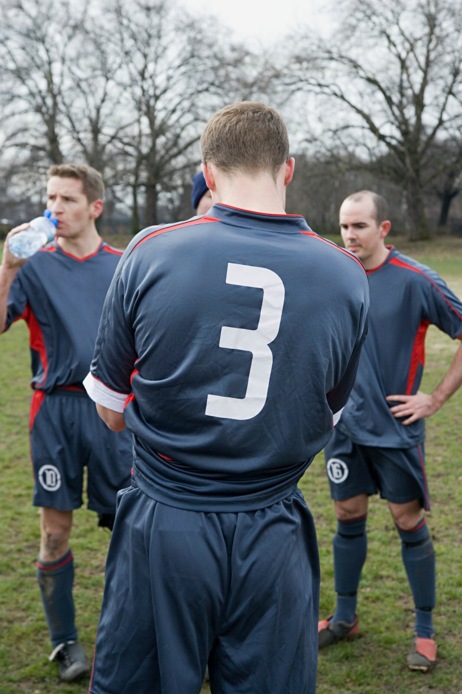 Football players in custom navy uniforms resting and hydrating during practice — bulk sports uniform manufacturer USA